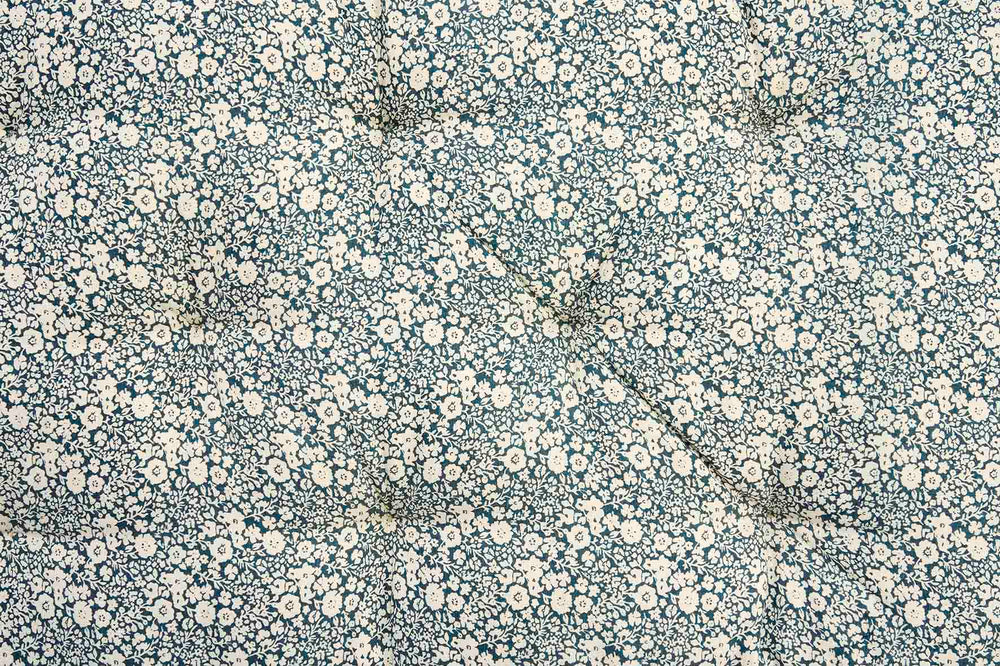 A close-up of a fabric surface with a dense small floral print in off-white and cream on a muted blue-gray background.