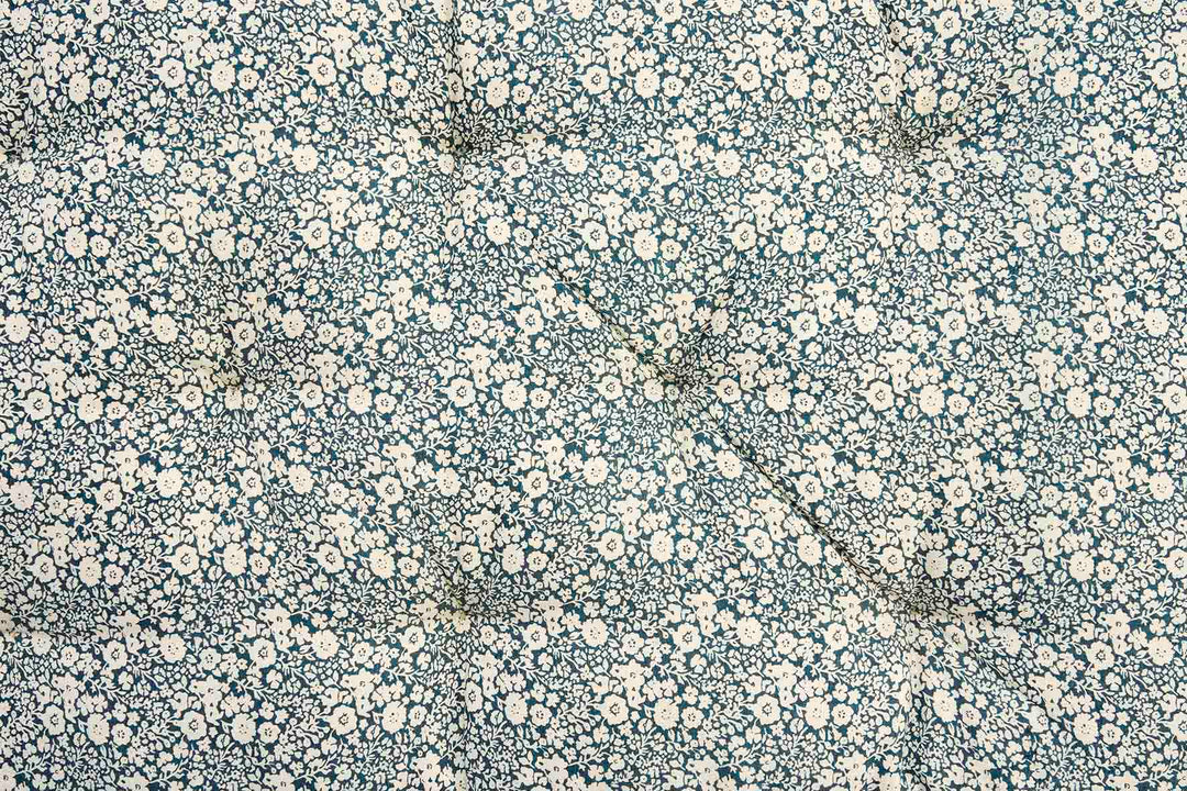 A close-up of a fabric surface with a dense small floral print in off-white and cream on a muted blue-gray background.