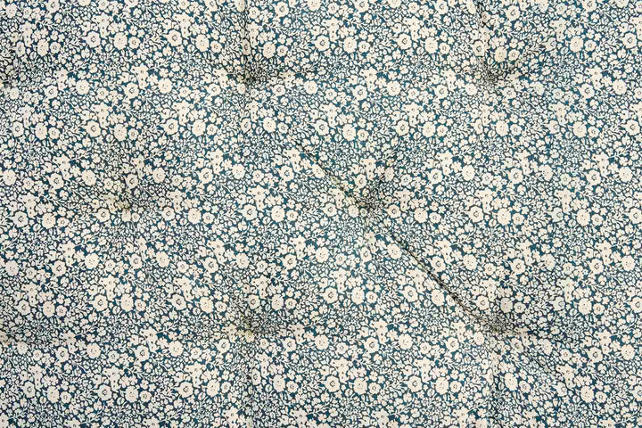 A close-up of a fabric surface with a dense small floral print in off-white and cream on a muted blue-gray background.