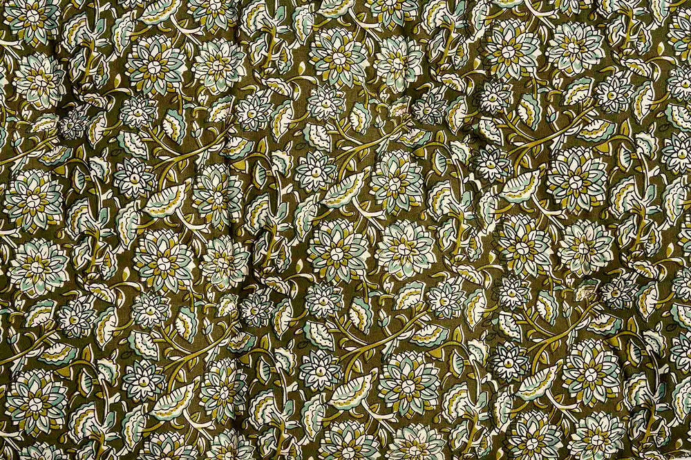 A close-up of a repeating floral pattern with white and light beige flowers, olive green leaves, and stems on a dark olive-brown background.