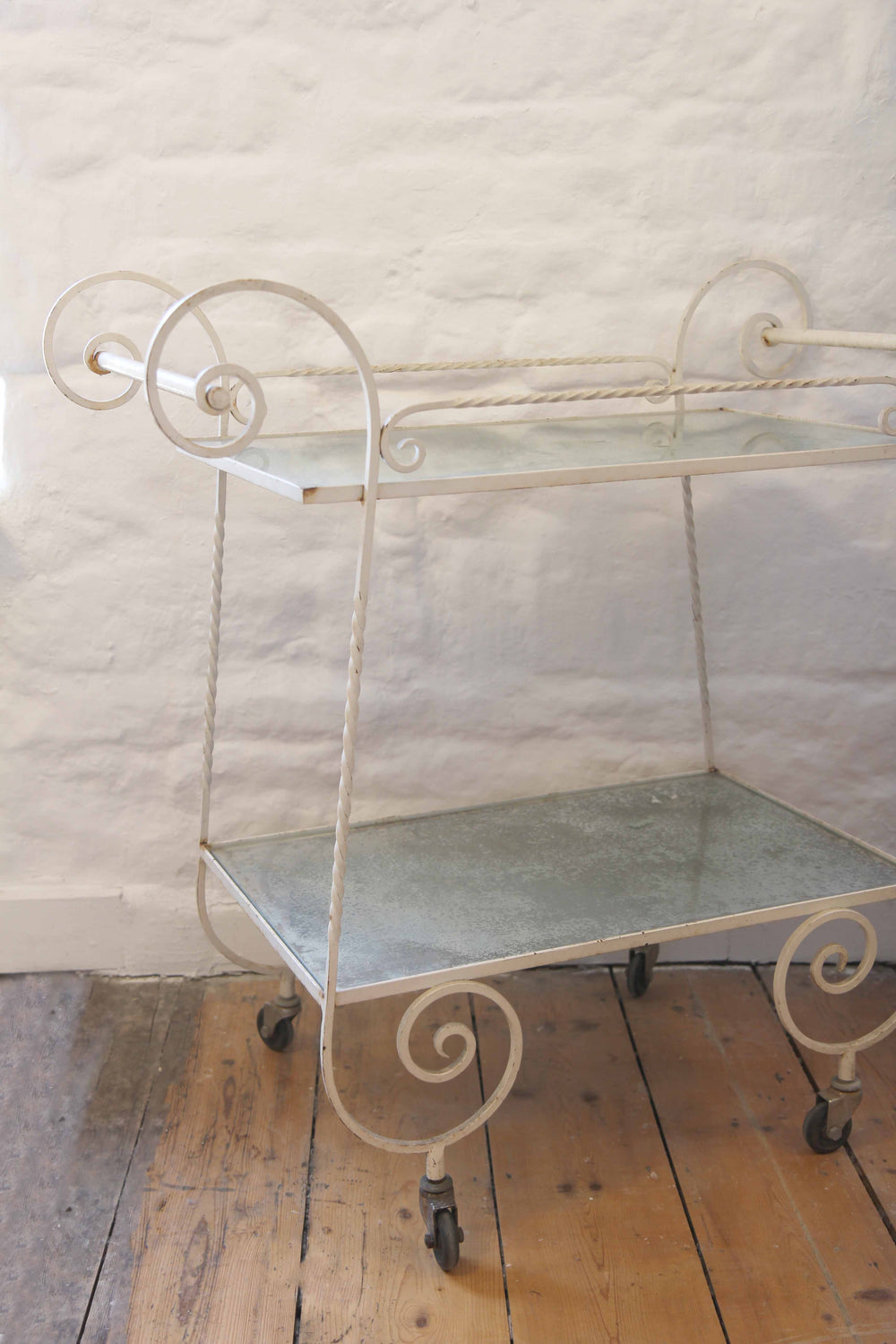 Vintage-style metal serving cart with glass shelves on a wooden floor.