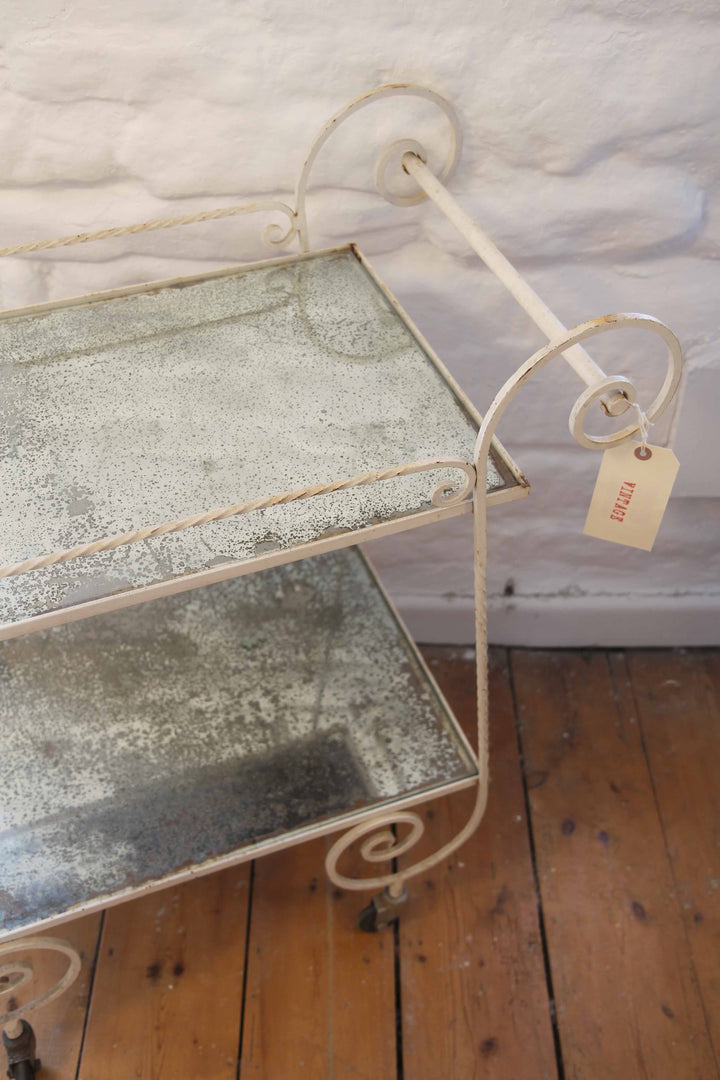 Vintage-style metal serving cart with distressed glass shelves on a wooden floor.