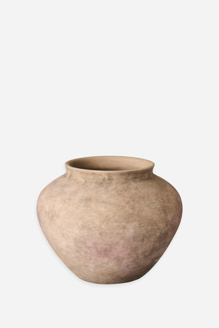 A rustic, rounded terracotta pot with a textured, earthy finish in shades of beige and light brown, set against a plain light gray background.