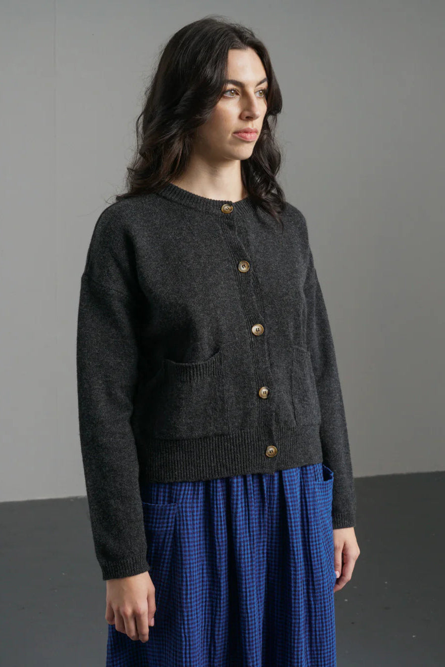 Woman wearing a dark gray cardigan over a blue dress against a plain background
