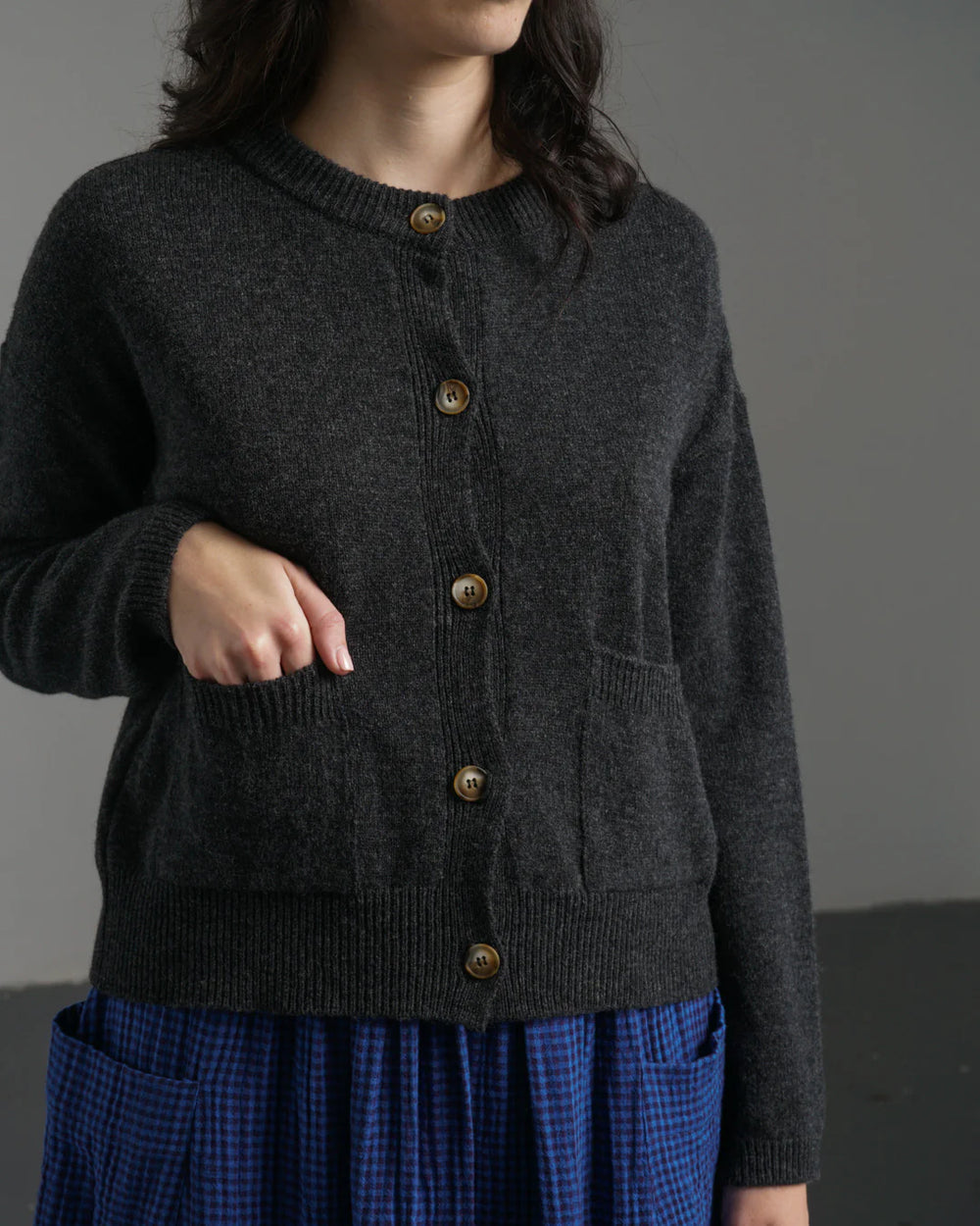 Person wearing a dark gray cardigan with gold buttons against a plain background
