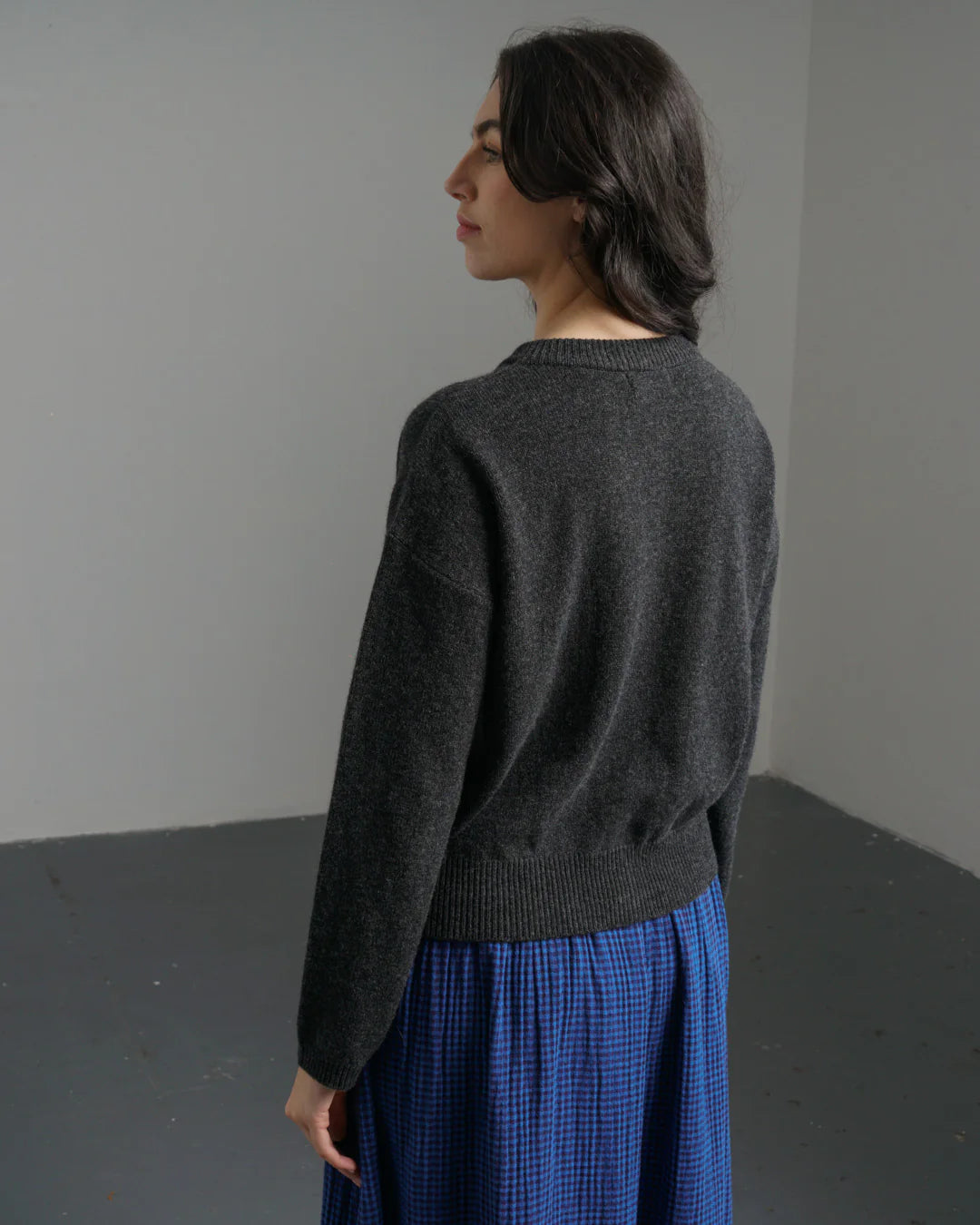 Person wearing a dark gray sweater and blue plaid skirt against a plain background