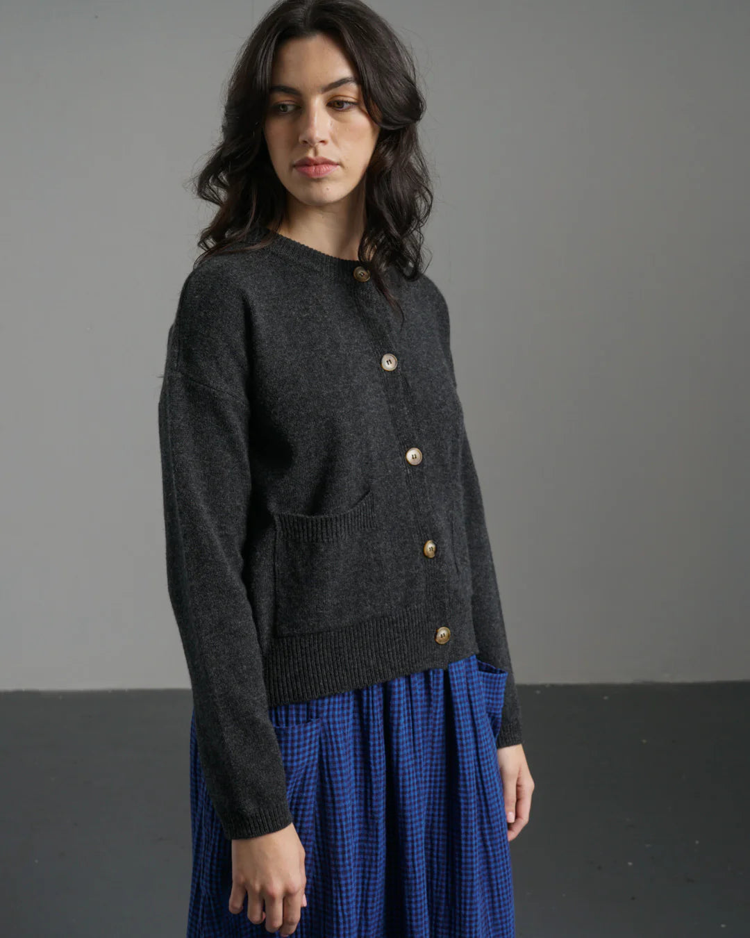 Woman wearing a dark gray sweater with gold buttons against a plain background
