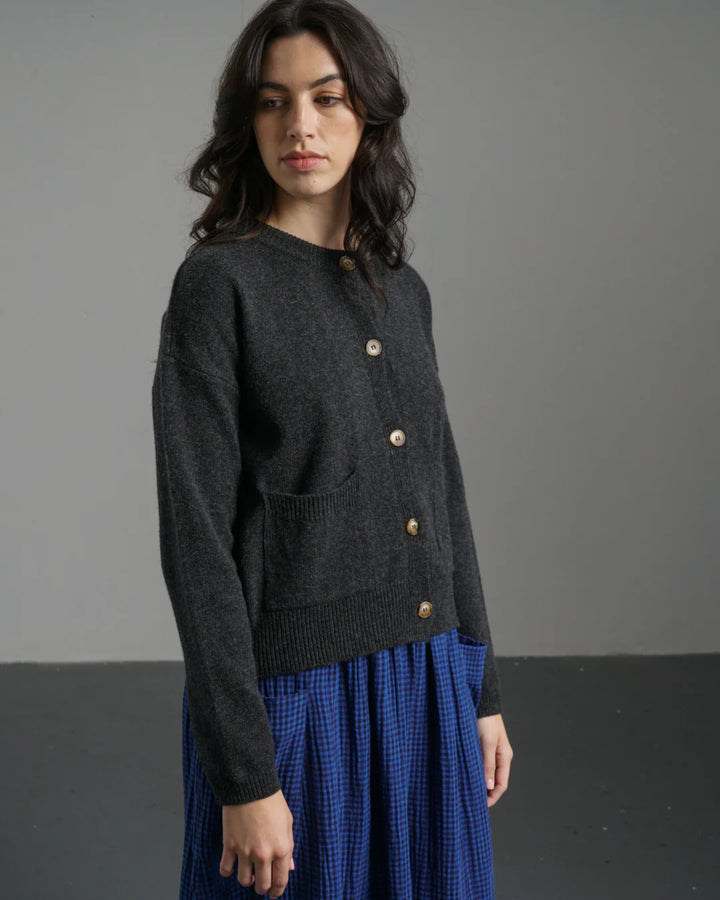 Woman wearing a dark gray sweater with gold buttons against a plain background