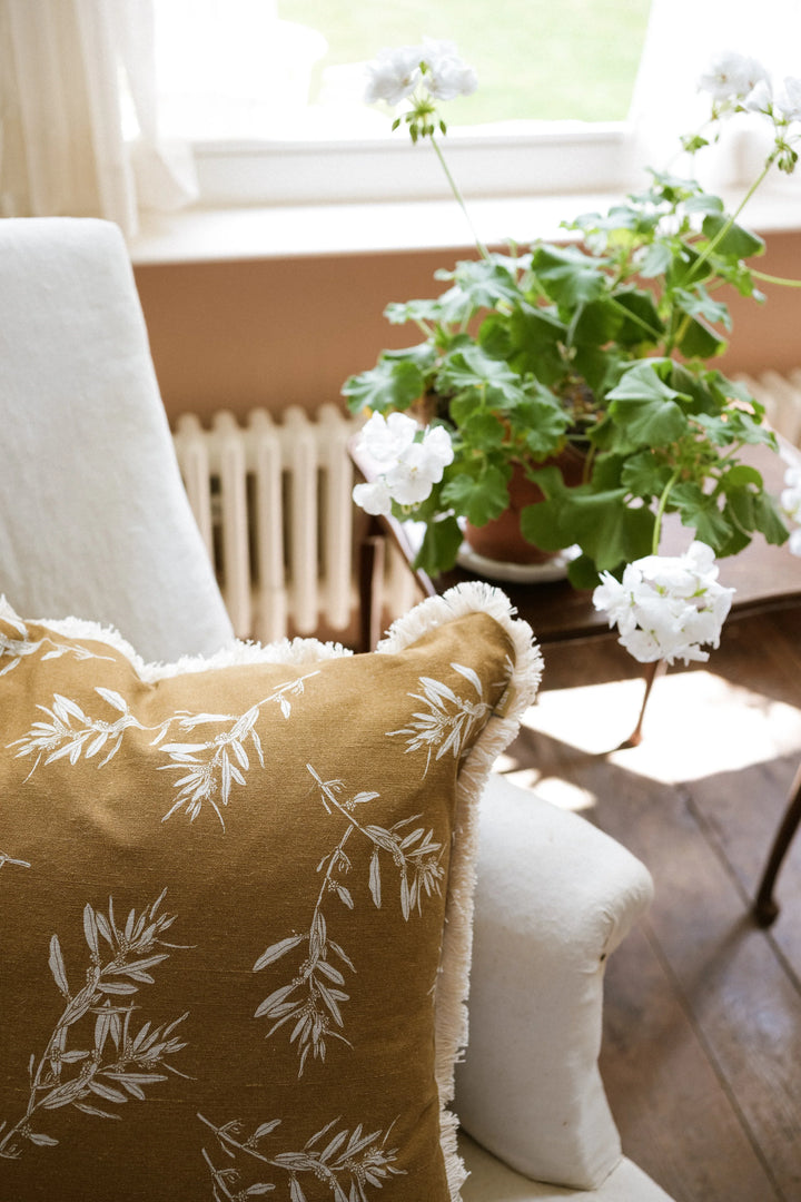 Decorative pillow with floral pattern on a couch next to a potted plant in a sunlit room.
