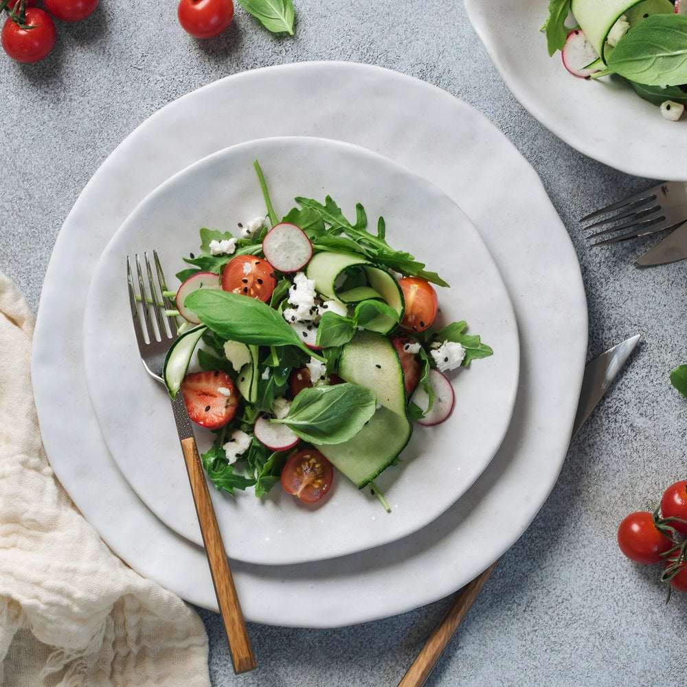 Salad with cucumbers, tomatoes, and radishes on a white plate with a fork.