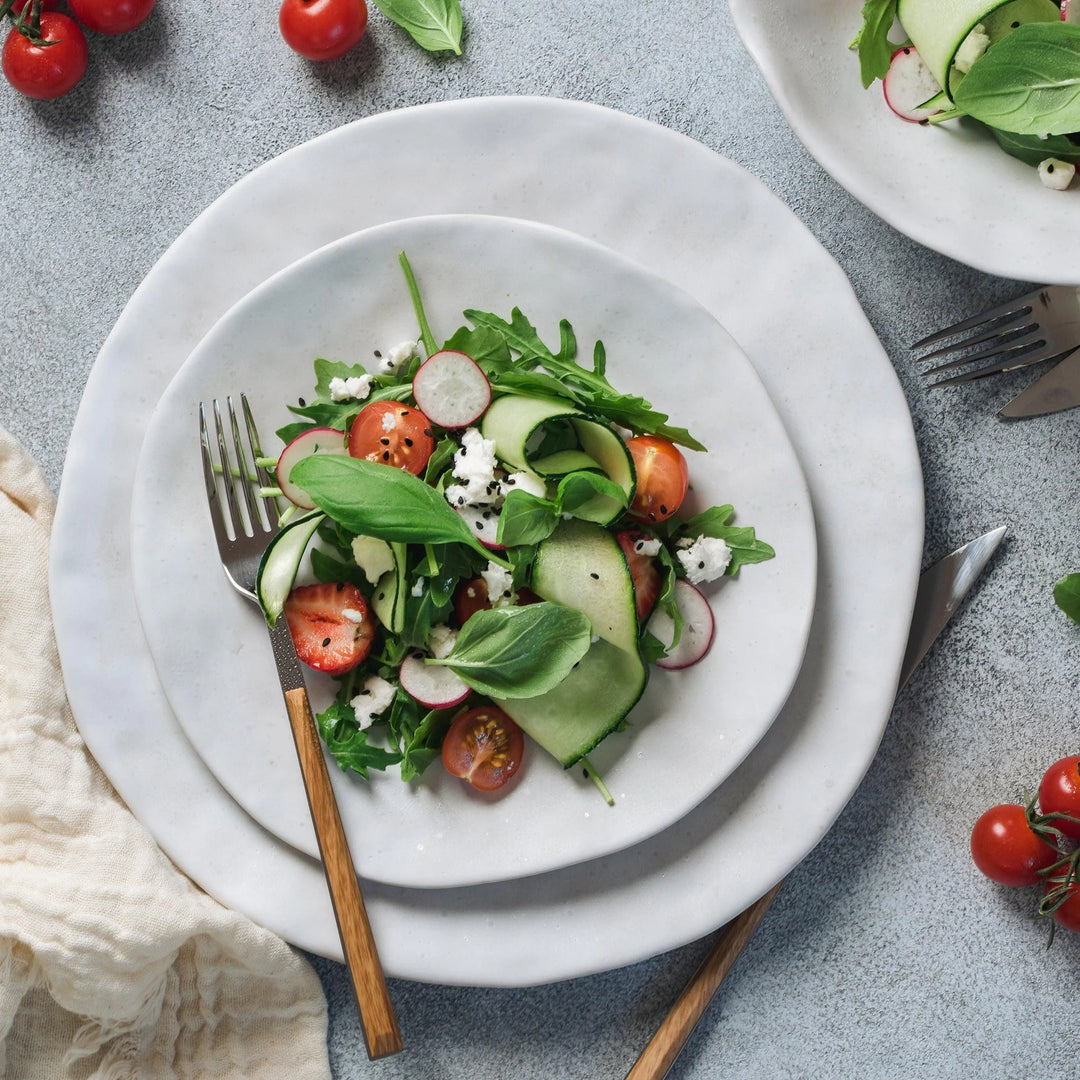 Salad with cucumbers, tomatoes, and radishes on a white plate with a fork.