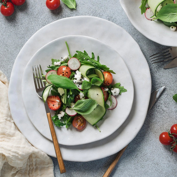 Salad with cucumbers, tomatoes, and radishes on a white plate with a fork.