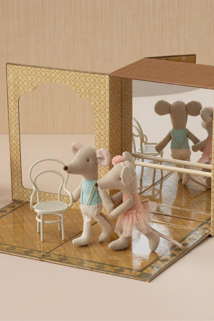 Two toy mice in ballet costumes standing in front of a mirror with a chair and table reflection.