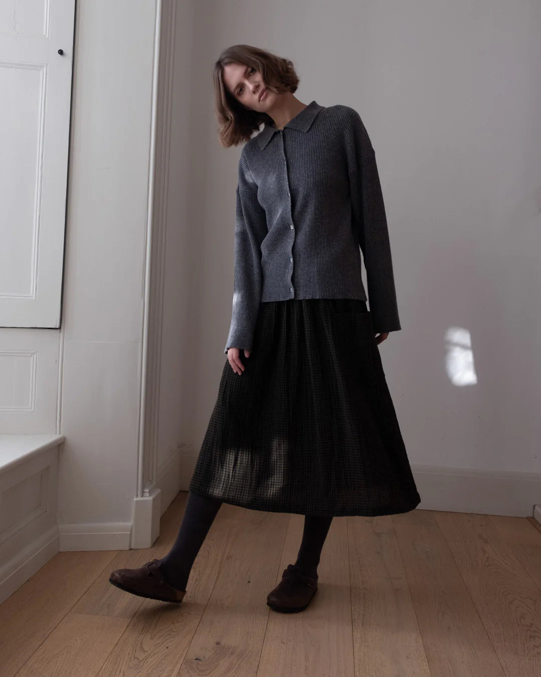 Woman wearing a dark gray outfit with a black skirt in a minimal indoor setting