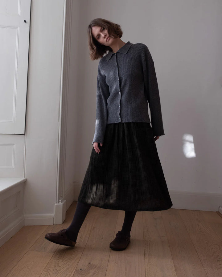 Woman wearing a dark gray outfit with a black skirt in a minimal indoor setting
