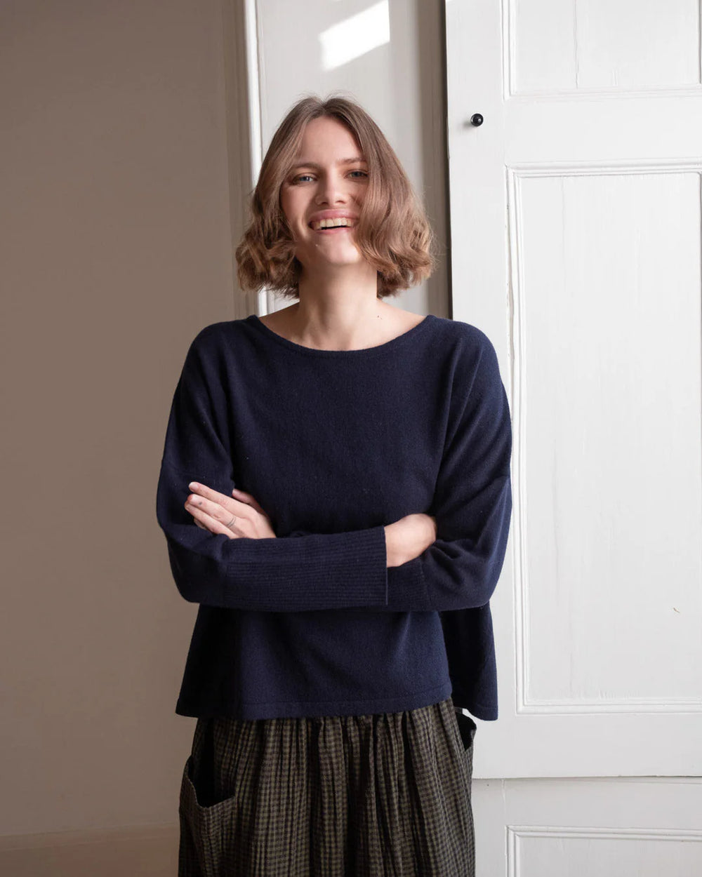 Woman wearing a navy blue sweater standing in a room with white walls.