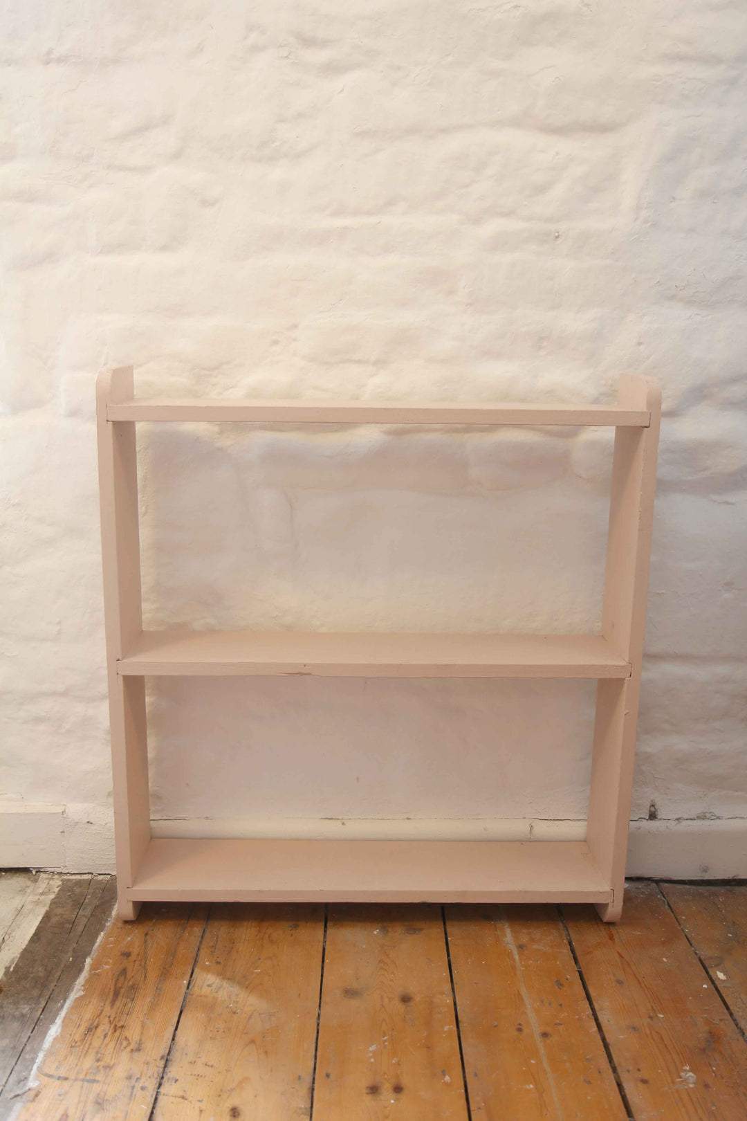 pink bookshelf against a textured white wall on a wooden floor