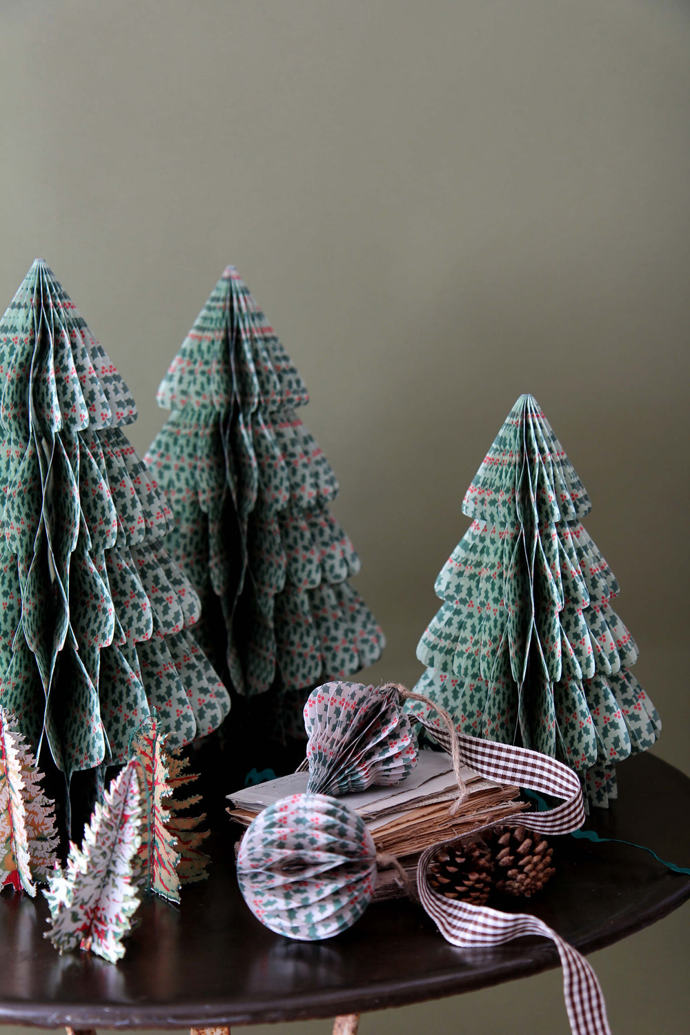 Small paper Christmas trees and decorative items on a table against a plain background