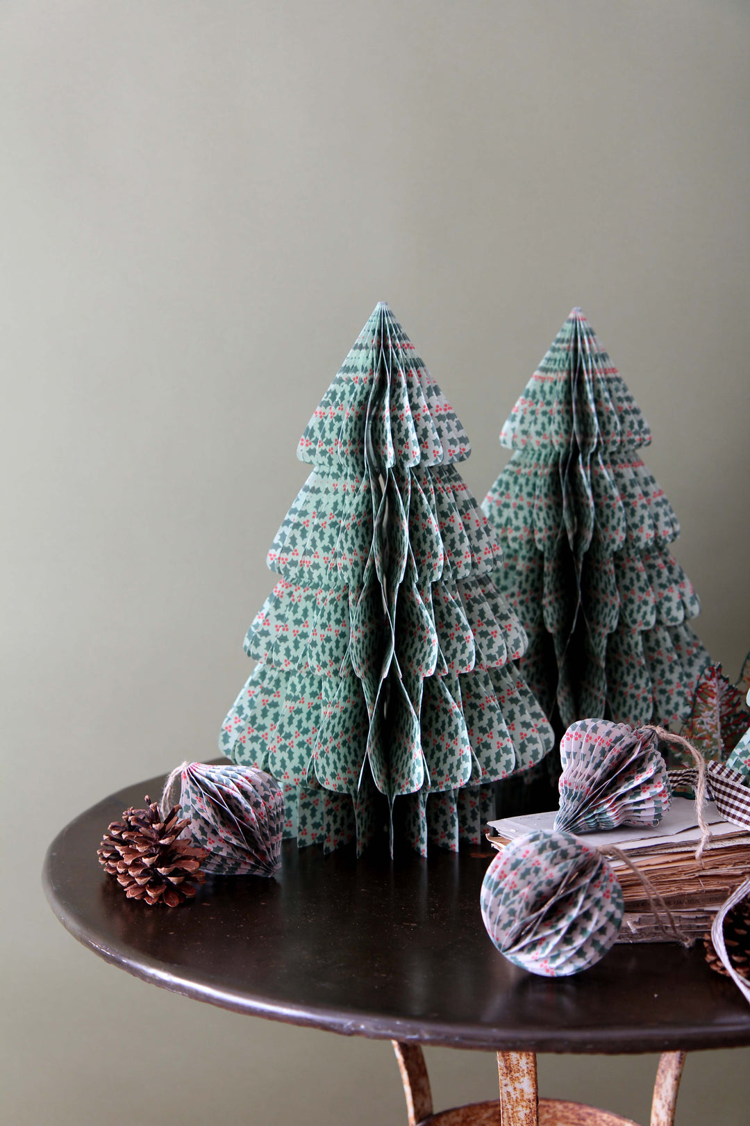 Decorative paper Christmas trees on a wooden table with pine cones and a basket.
