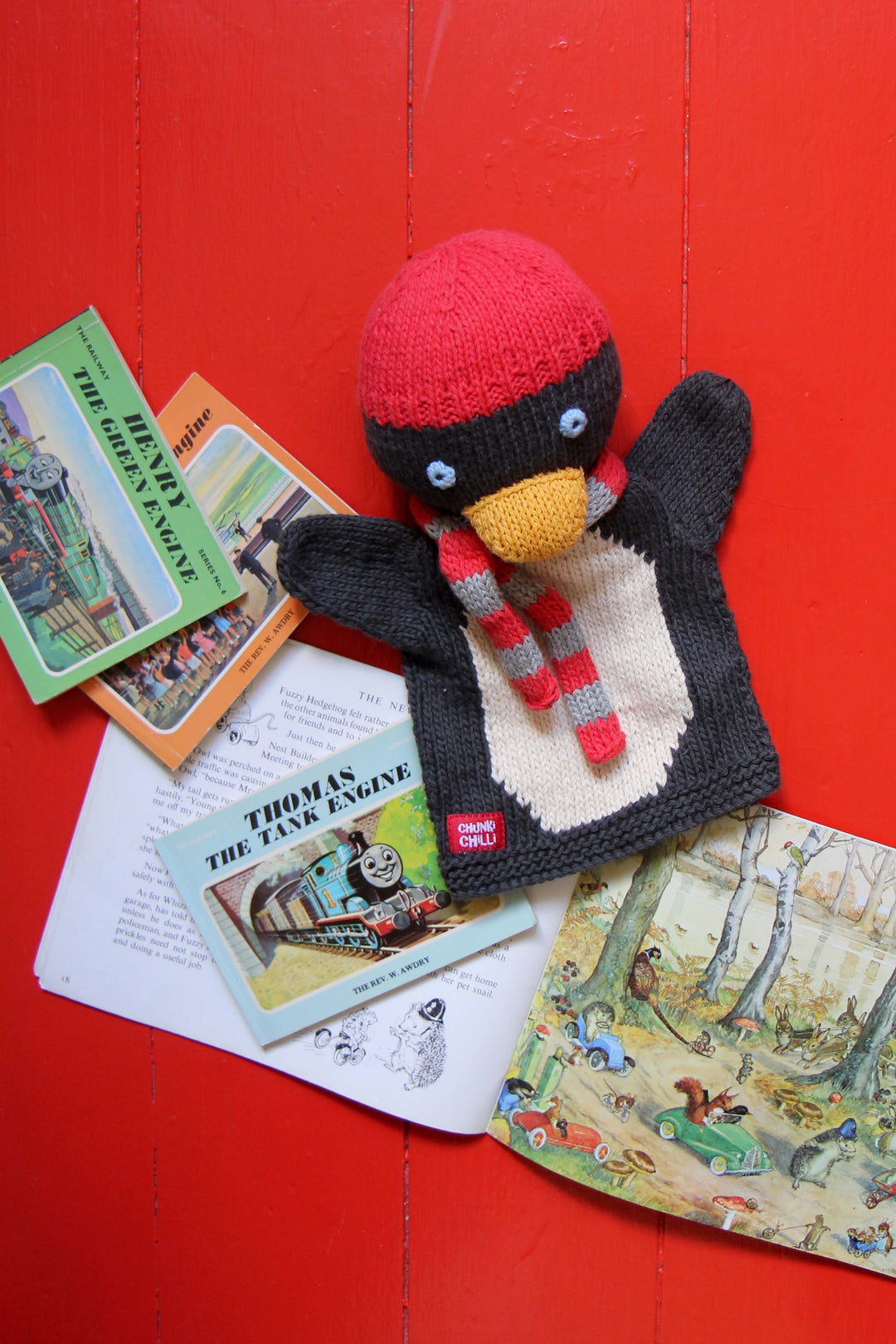 Knitted penguin toy with a red hat and scarf on a red background with vintage books.