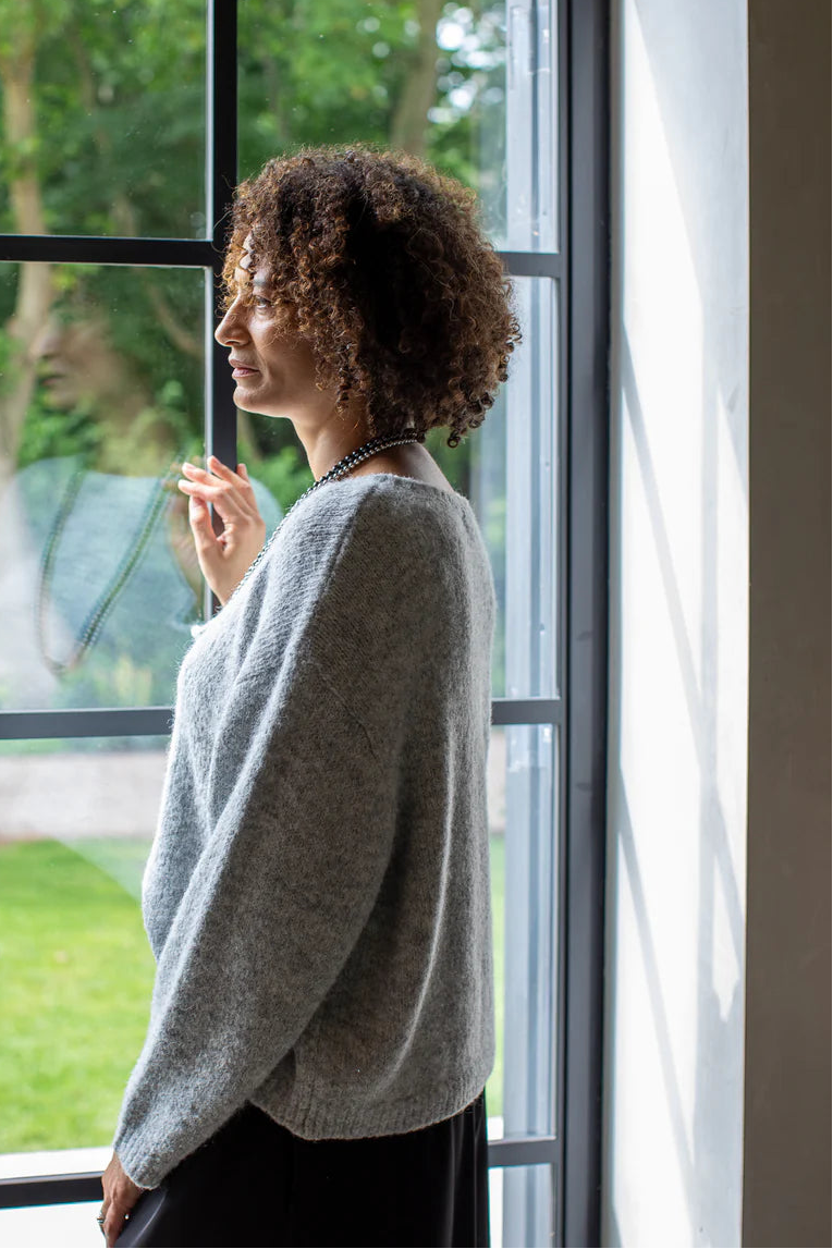 Woman standing by a large window looking outside at a garden.
