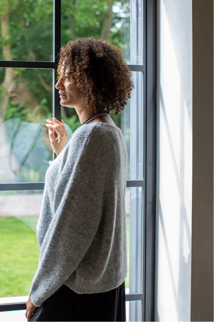 Woman standing by a large window looking outside at a garden.