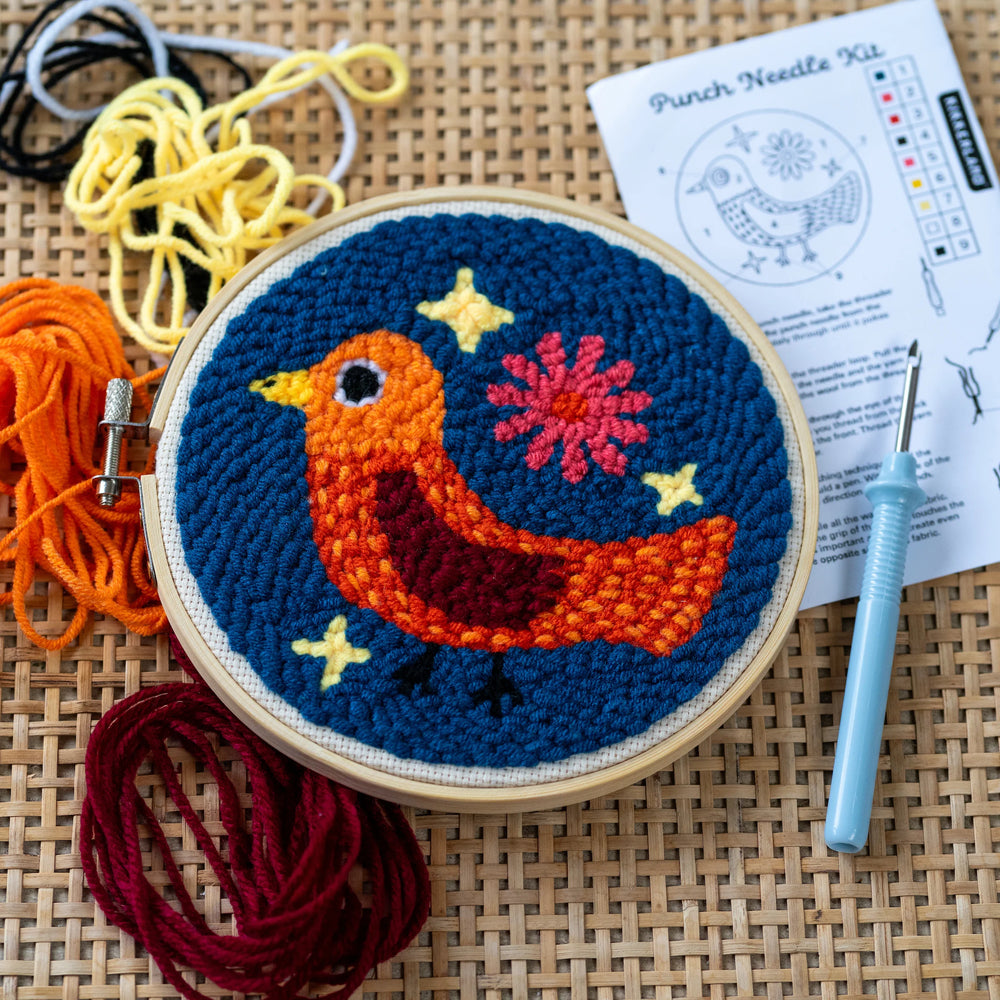Embroidery hoop with a colorful bird design on a woven surface with yarn and instructions.