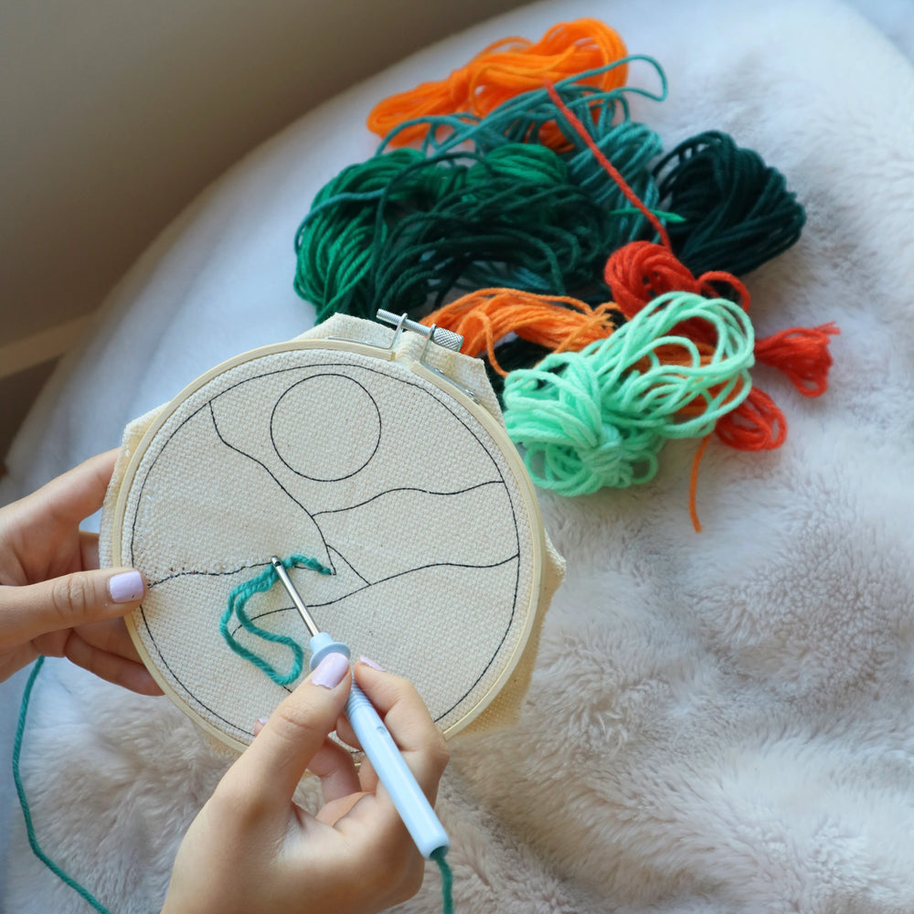Person embroiderying a design on fabric with colorful threads in the background
