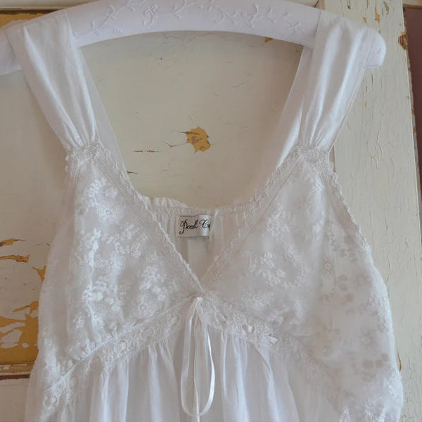 White lace dress on a hanger with a visible brand label against a rustic wooden background.