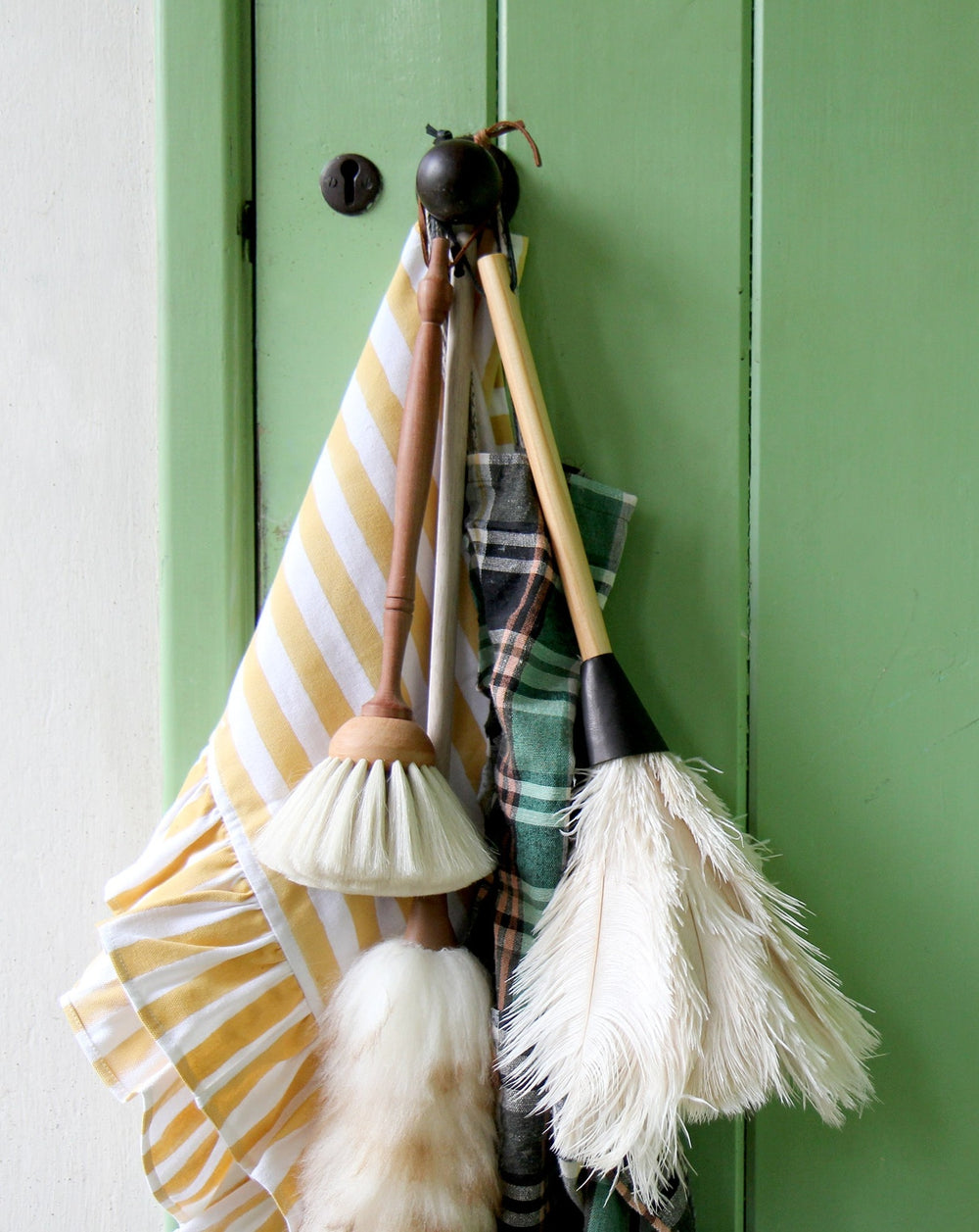 short ostrich feather duster with wooden handle and cream feathers, pictured against green pantry door with other brushes and t-towels