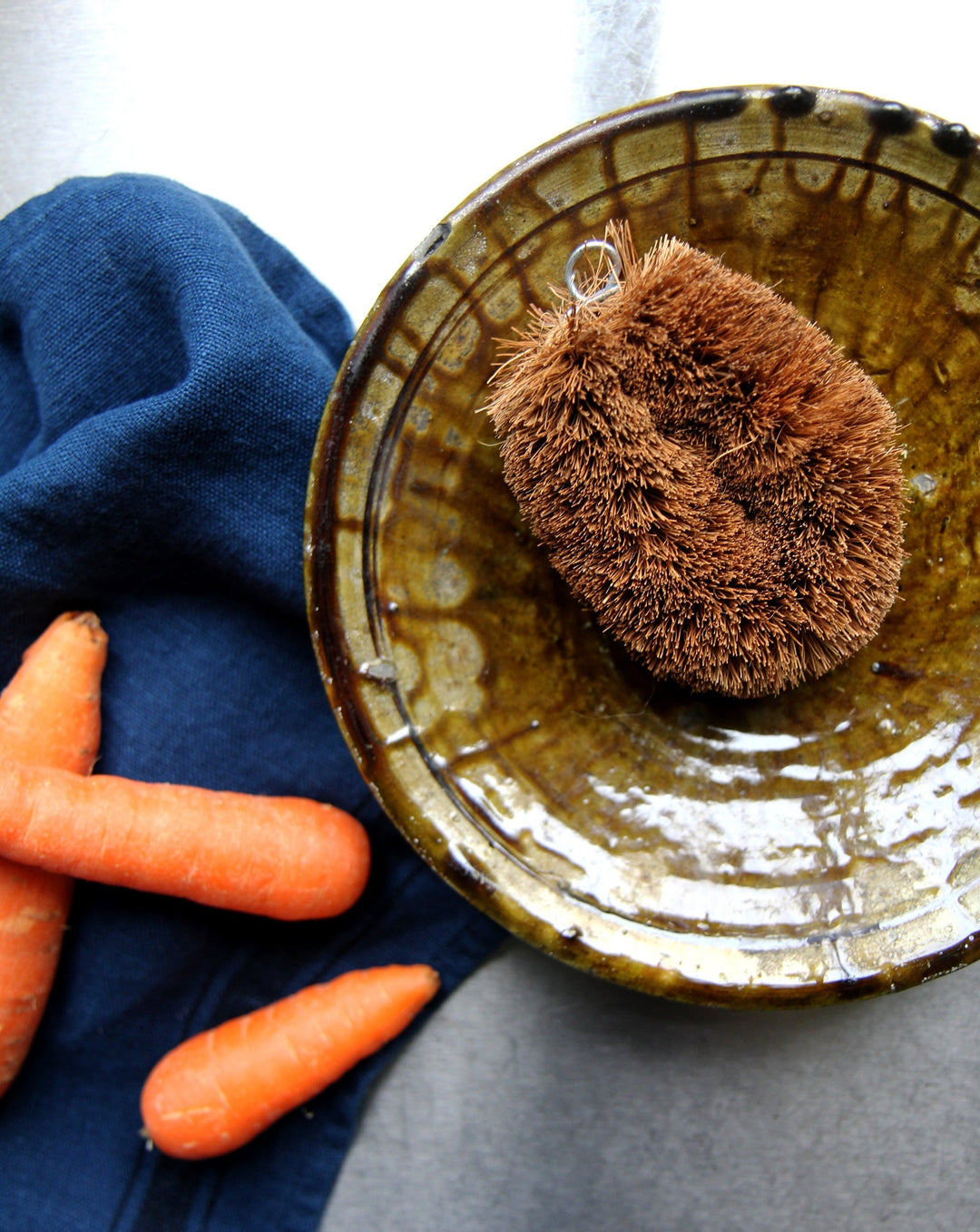 redecker coconut fibre brush for cleaning vegetables, say in a tamagroute pottery bowl with t-towel and scattered carrots.
