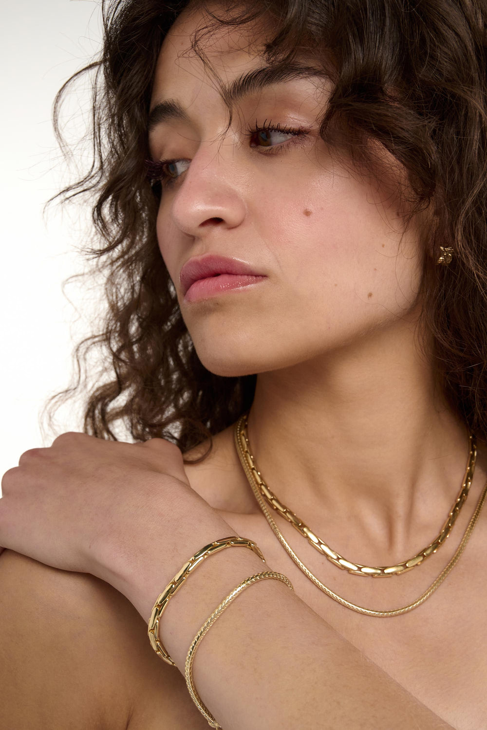 Woman wearing gold jewelry including a necklace and bracelets on a neutral background