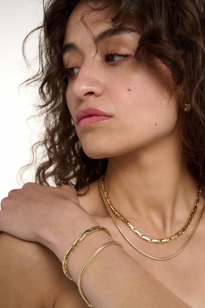 Woman wearing gold jewelry including a necklace and bracelets on a neutral background