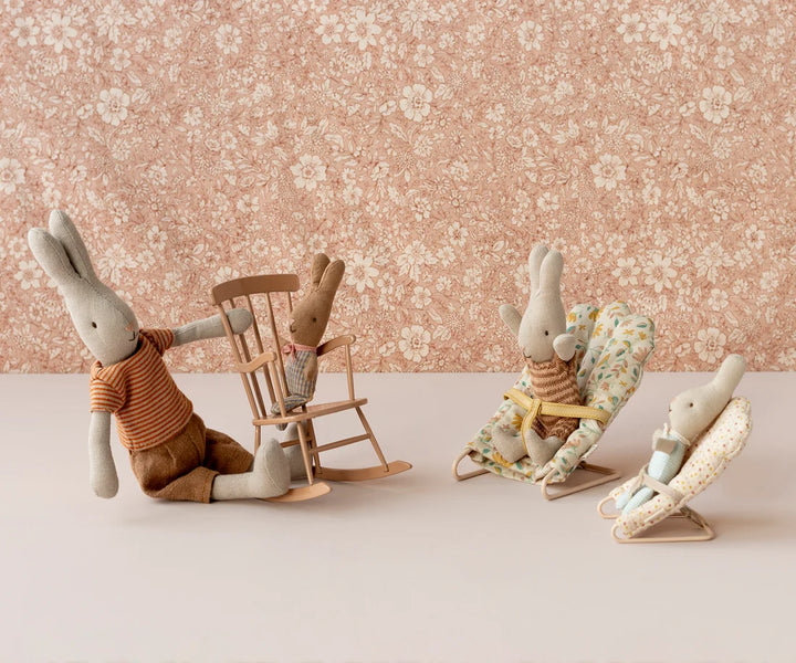 Three plush toy rabbits in various poses against a floral wallpaper background