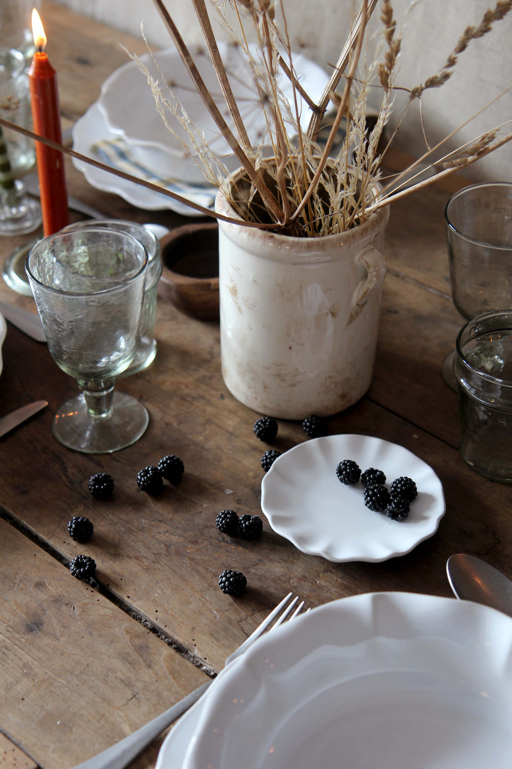 Dining table setting with blackberries, white plates, and a candle on a wooden surface.
