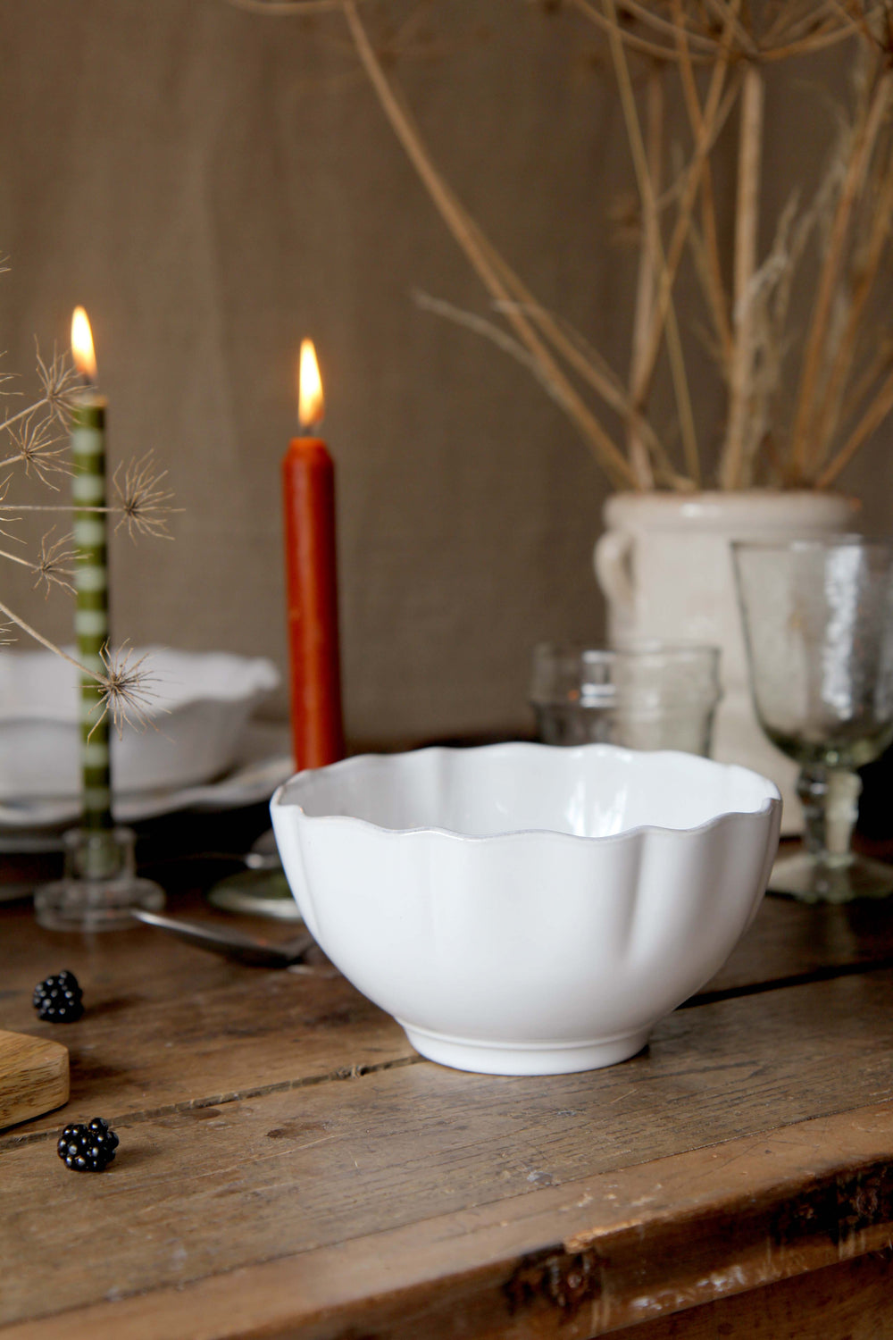 White rosa scalloped cereal bowl on a wooden table with candles 