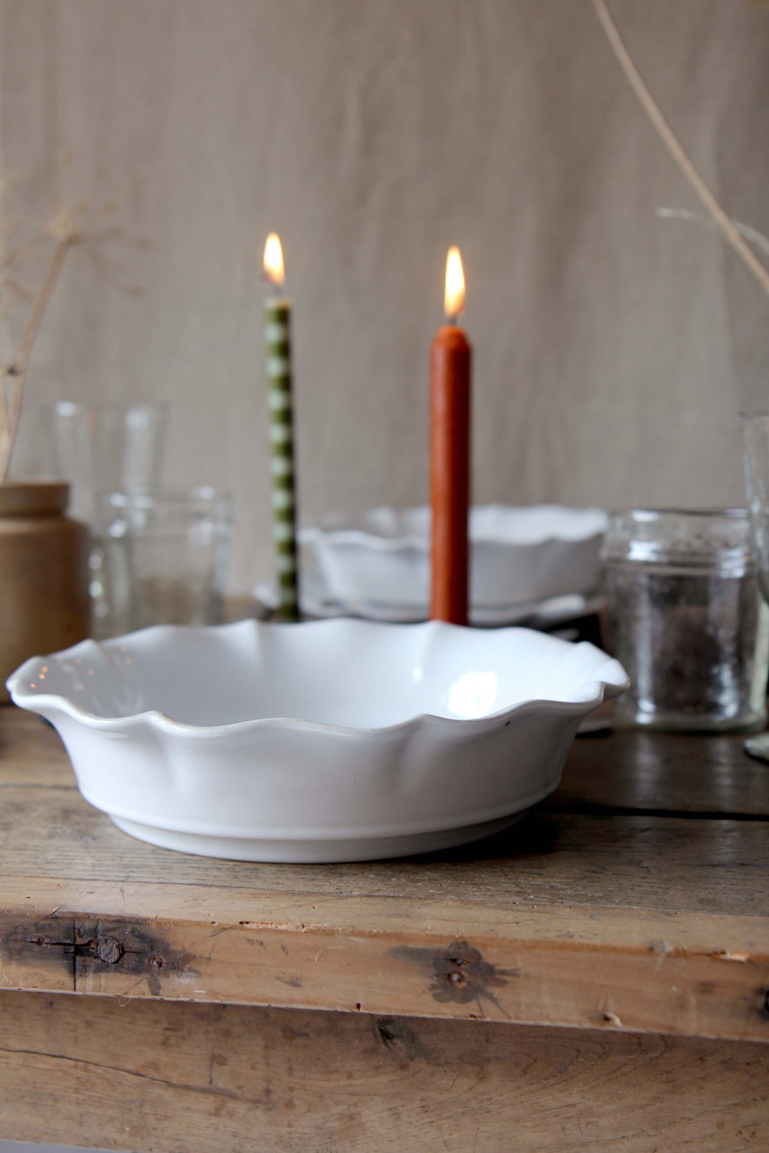 White rosa scalloped pasta plate on a wooden surface with candles and glasses in the background