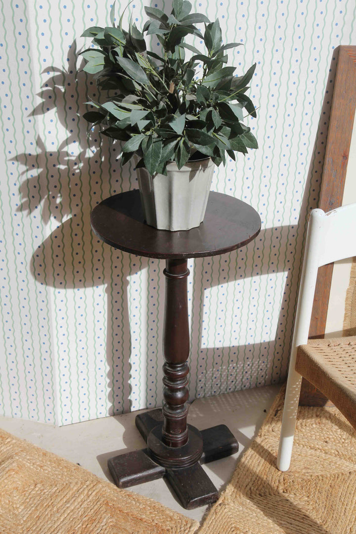 Small wooden table with a potted plant against a textured wall.