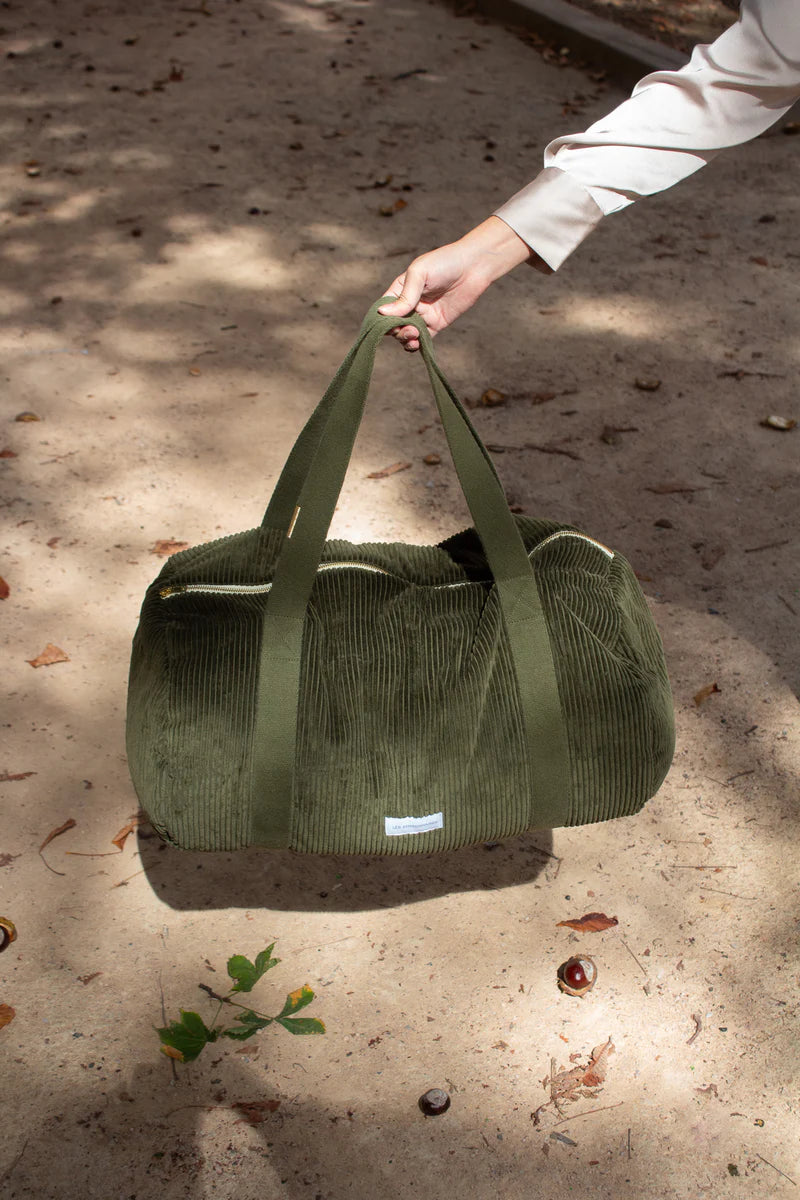 Green duffel bag being held by a person on a sandy surface.