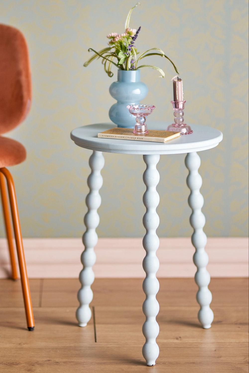 Small round white table with bobbin legs in a room setting with a chair and decorative items.