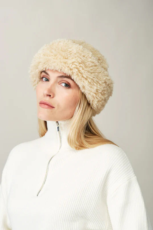 Woman wearing a beige knitted hat against a plain background