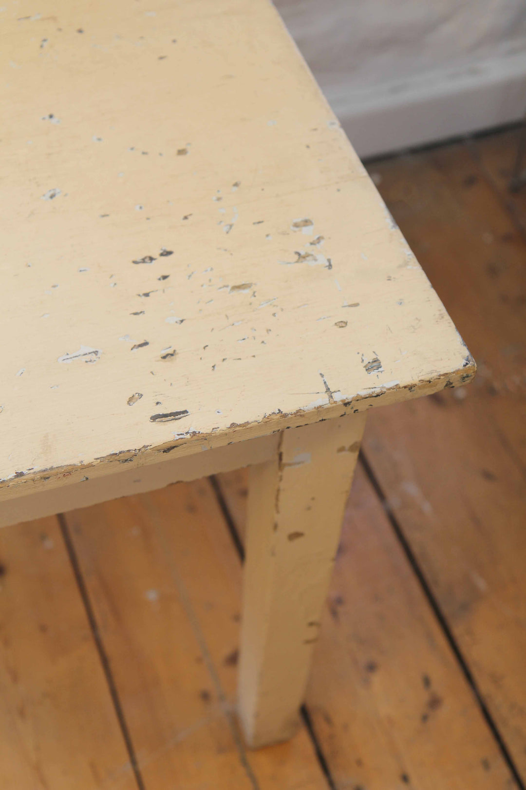 Close-up of a vintage wooden table with visible wear and tear on a wooden floor.