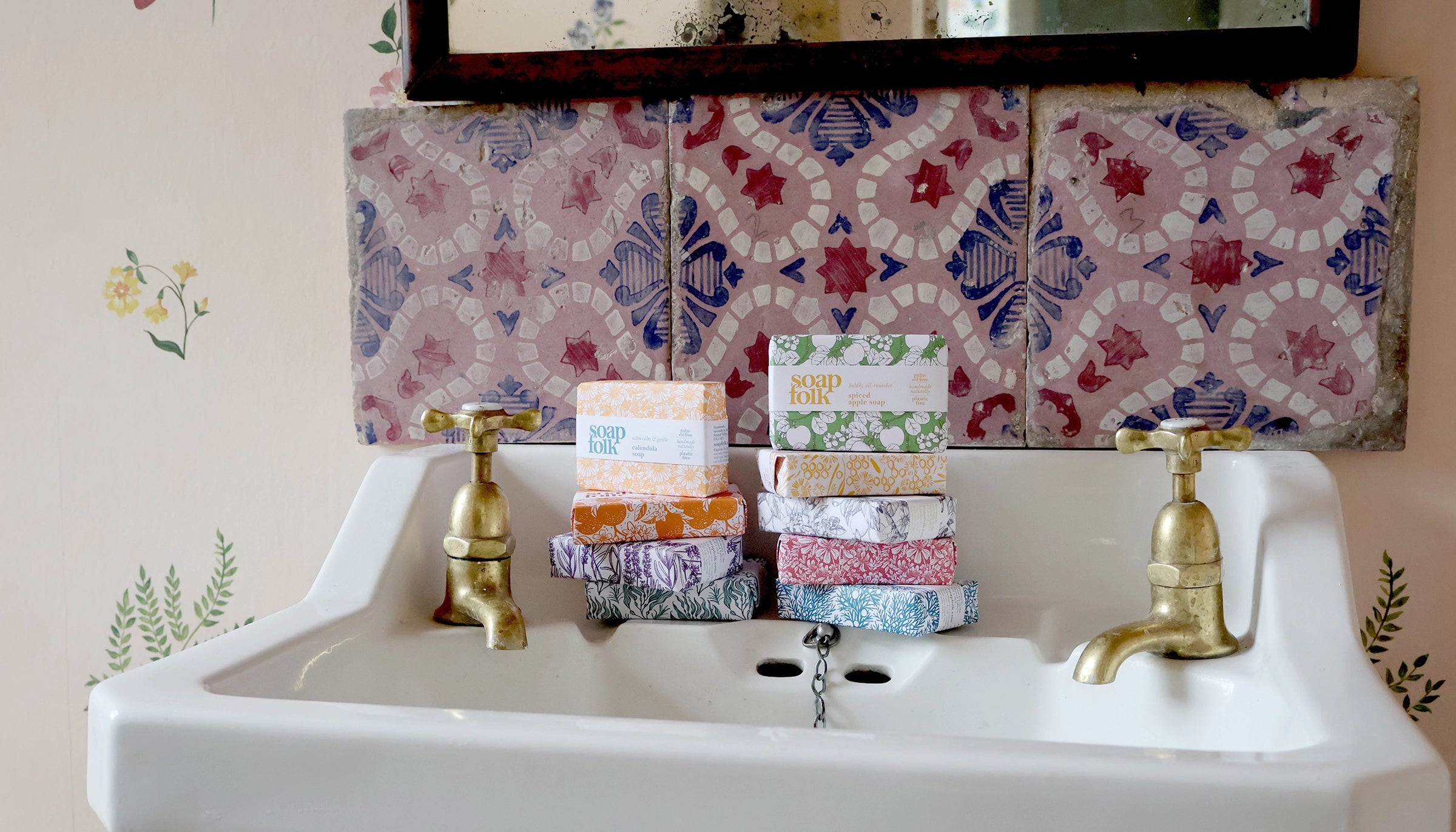 White sink with gold faucets, colorful soap bars, and a patterned tile backsplash.