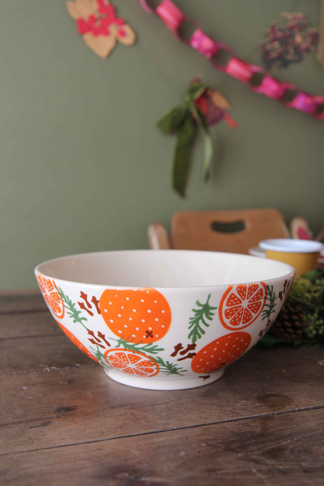 Decorative bowl with orange design on a wooden table against a green wall.