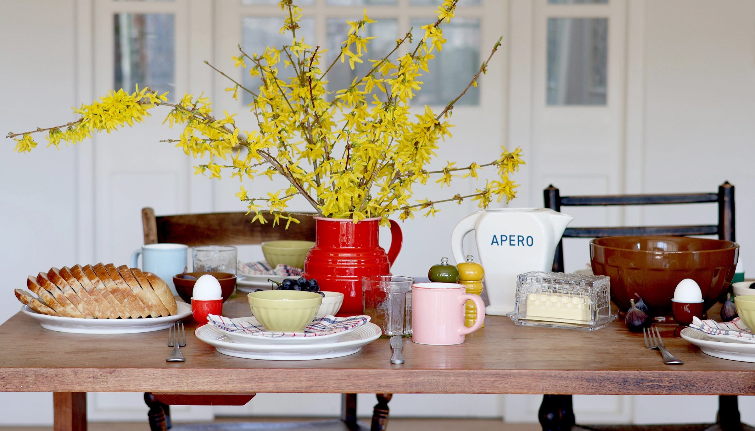 Dining table set with plates, cups, and a vase of yellow flowers.