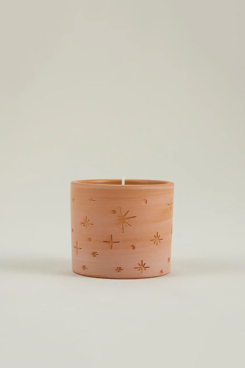 Terracotta candle pot with star patterns on a light beige background