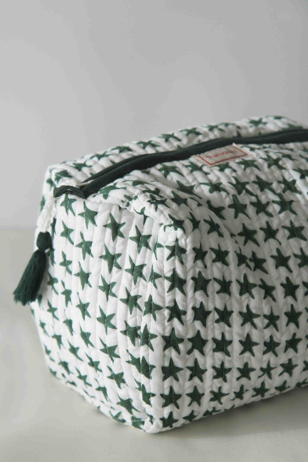 White pouch with green star pattern and black zipper on a light gray background