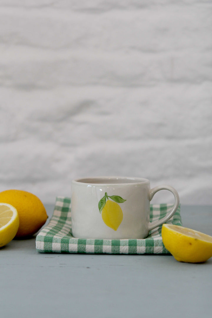 stoneware lemon mug with green gingham t-towel and cut lemons