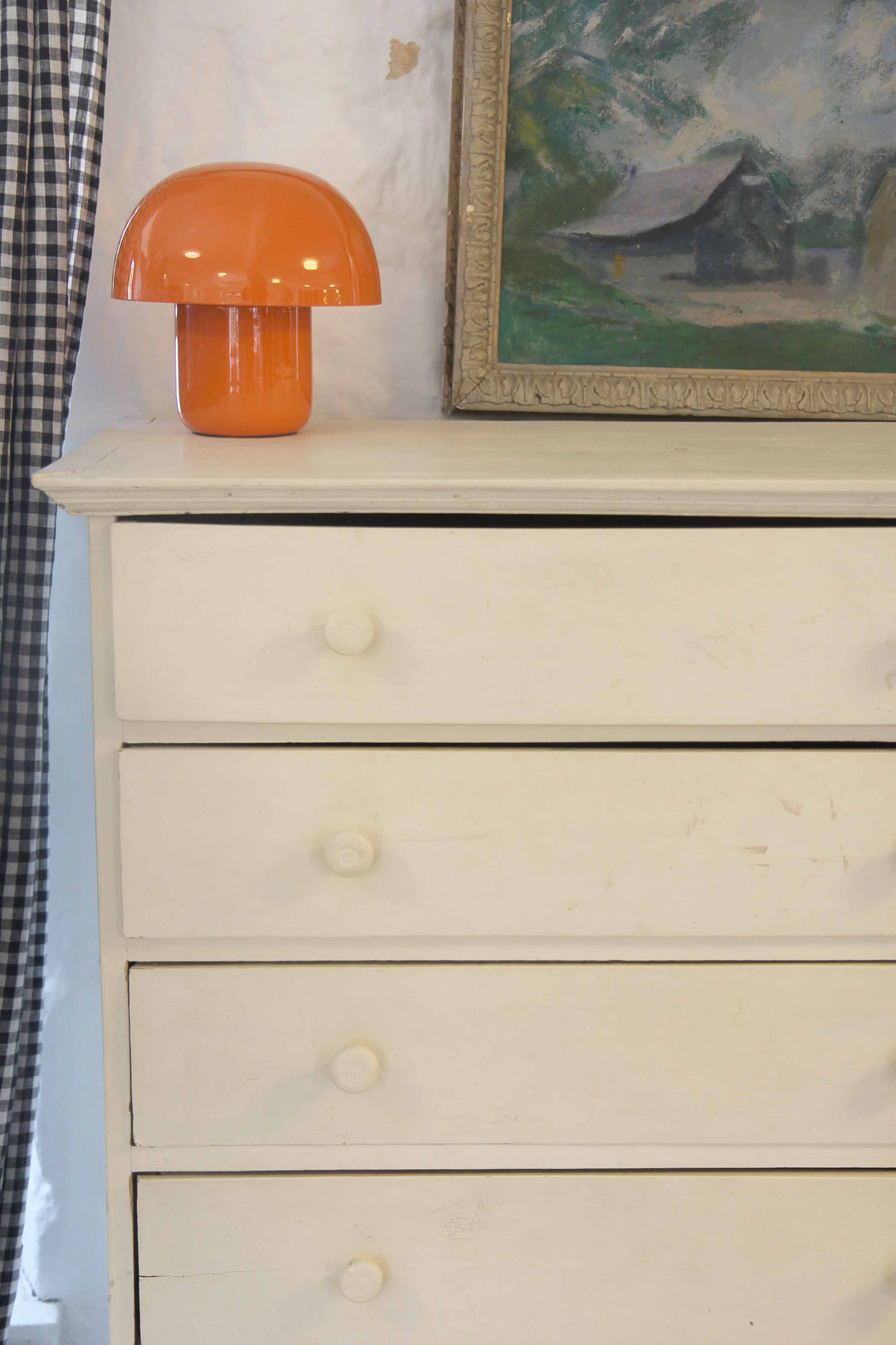 White dresser with an orange lamp and framed painting on top