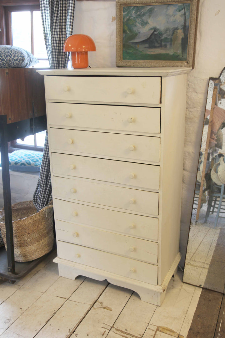 White dresser with orange lamp on top in a room with wooden floor and framed picture.